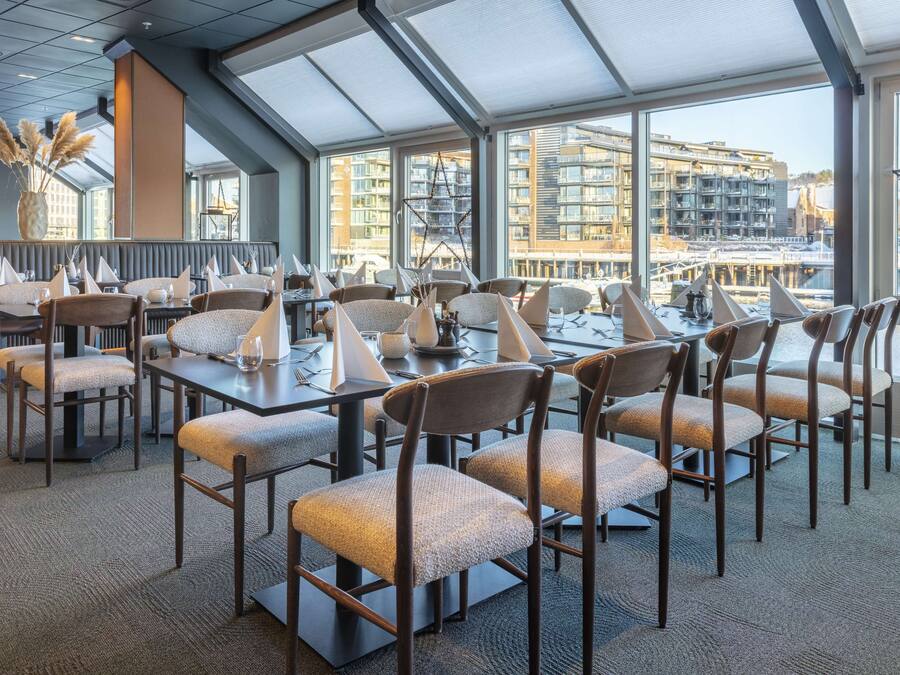 A modern dining area with high tables and chairs, large windows offering a view of the cityscape.