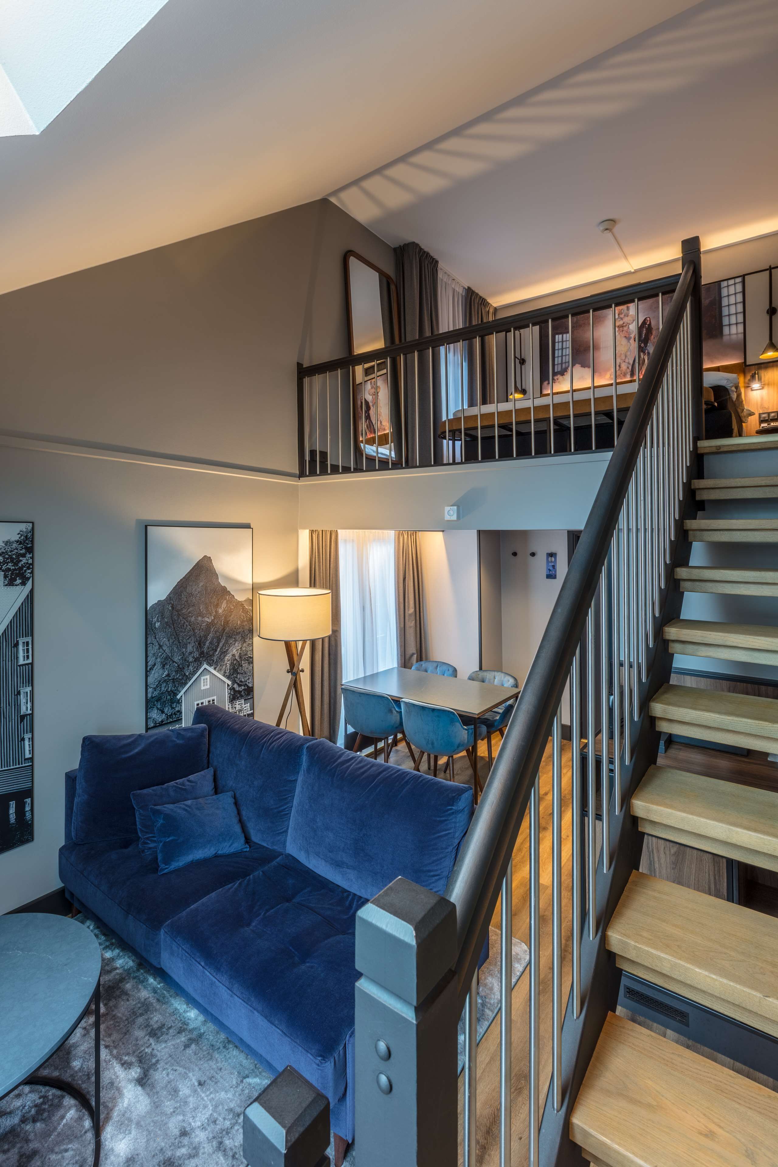 A modern living room with a blue sofa, a dining table, and a staircase leading to an upper level.
