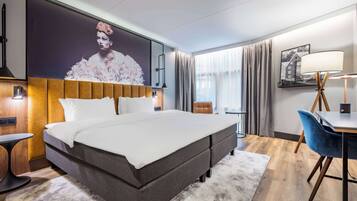 Una habitación de hotel con una cama grande, un escritorio con silla, una lámpara y un cartel grande en la pared.
