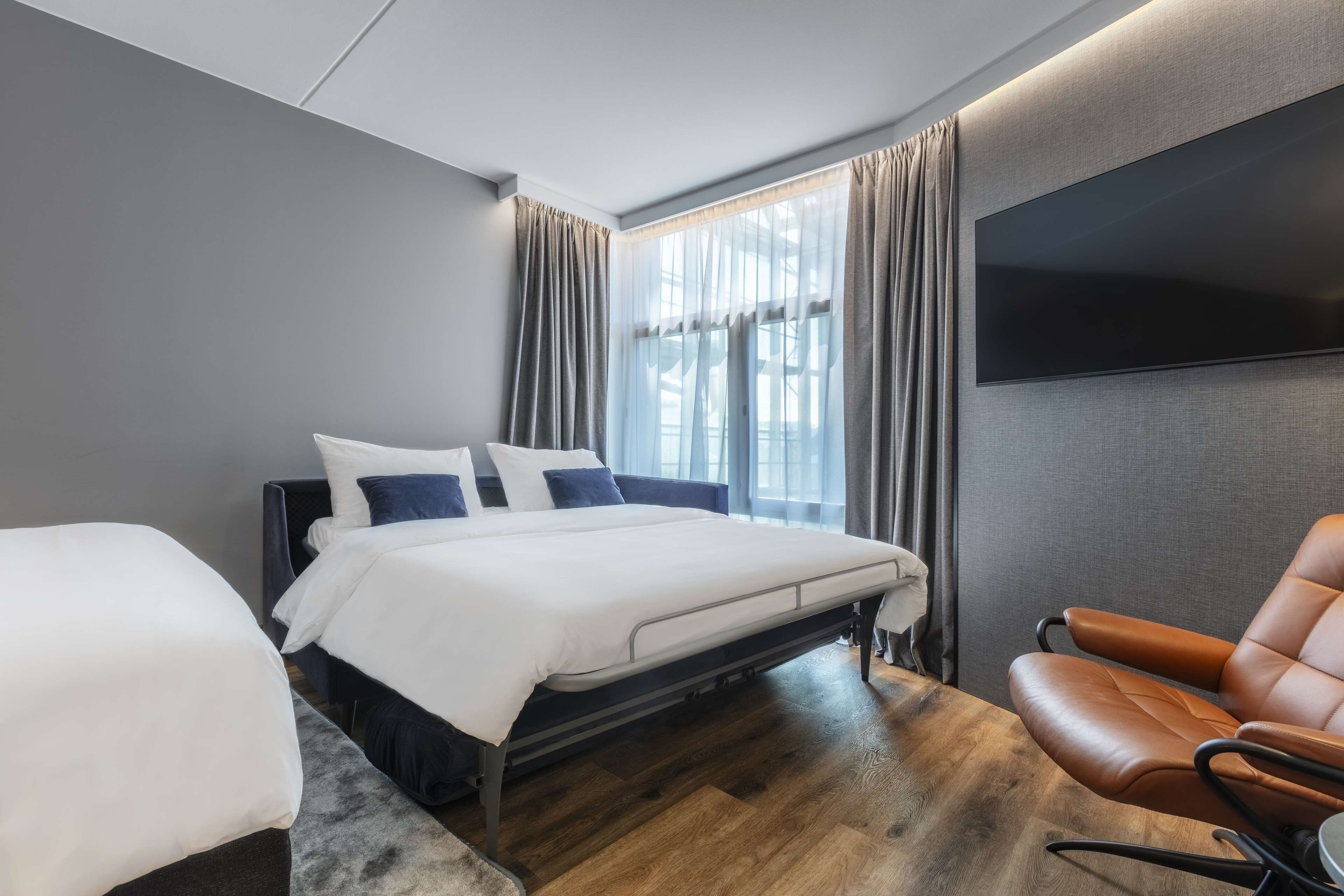 Una habitación de hotel moderna con una cama grande, un sofá y un televisor de pantalla plana montado en la pared.