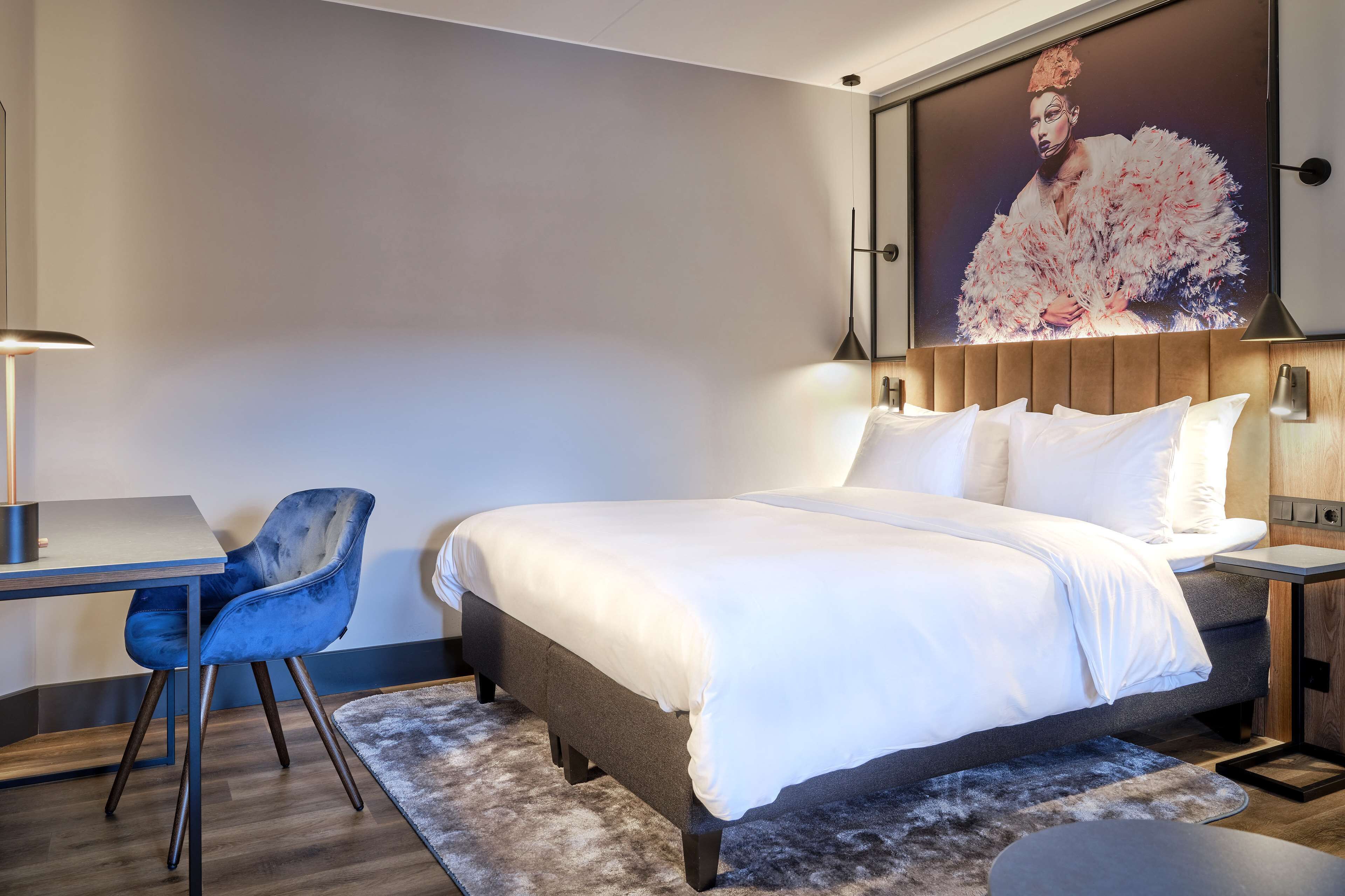 A modern hotel room with a large bed, a desk, and a chair.