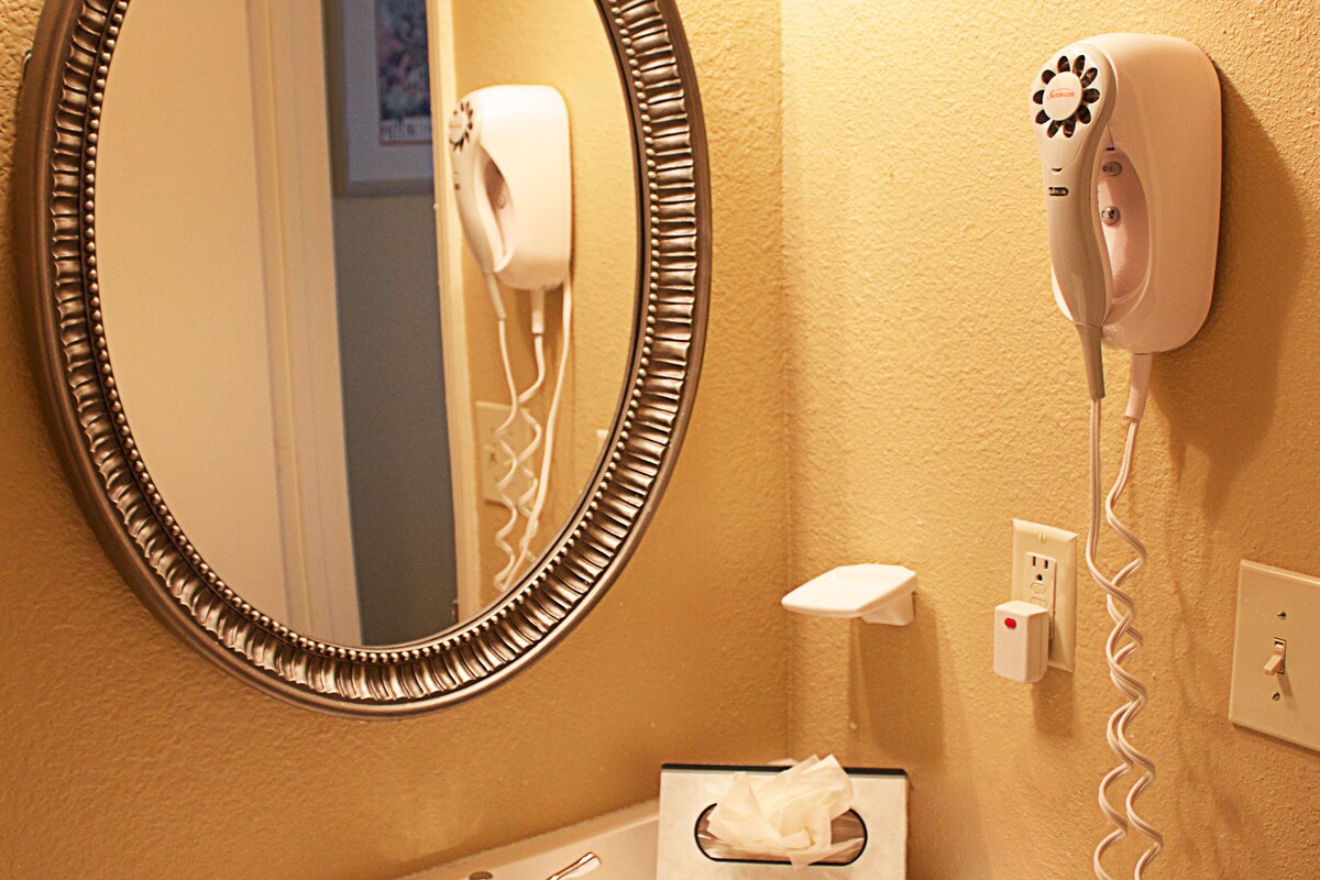A bathroom with a sink, mirror, hairdryer, and toiletries.