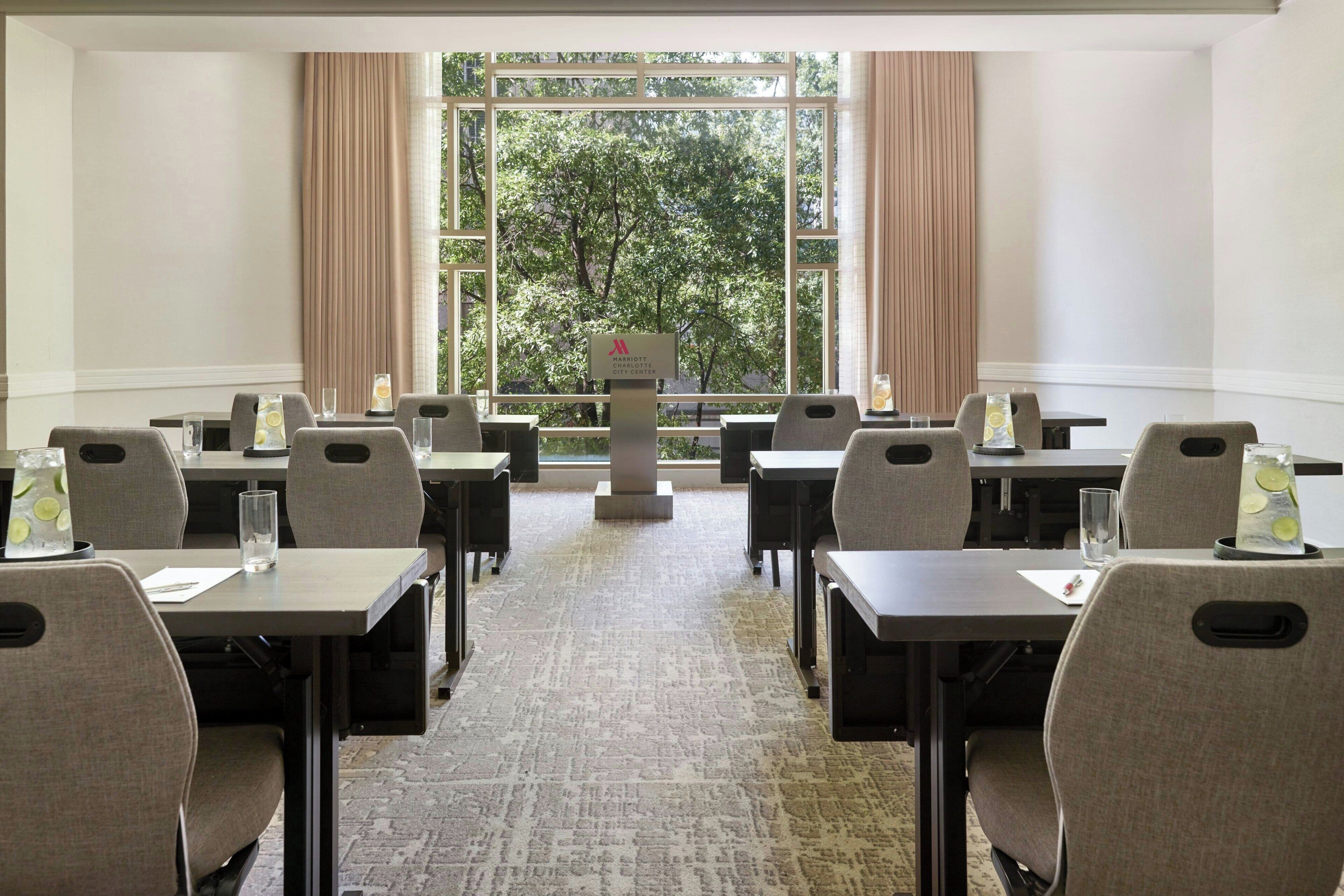 A conference room with tables and chairs, a large window with a view of trees, and a sign indicating it's part of the Marriott Hotel.