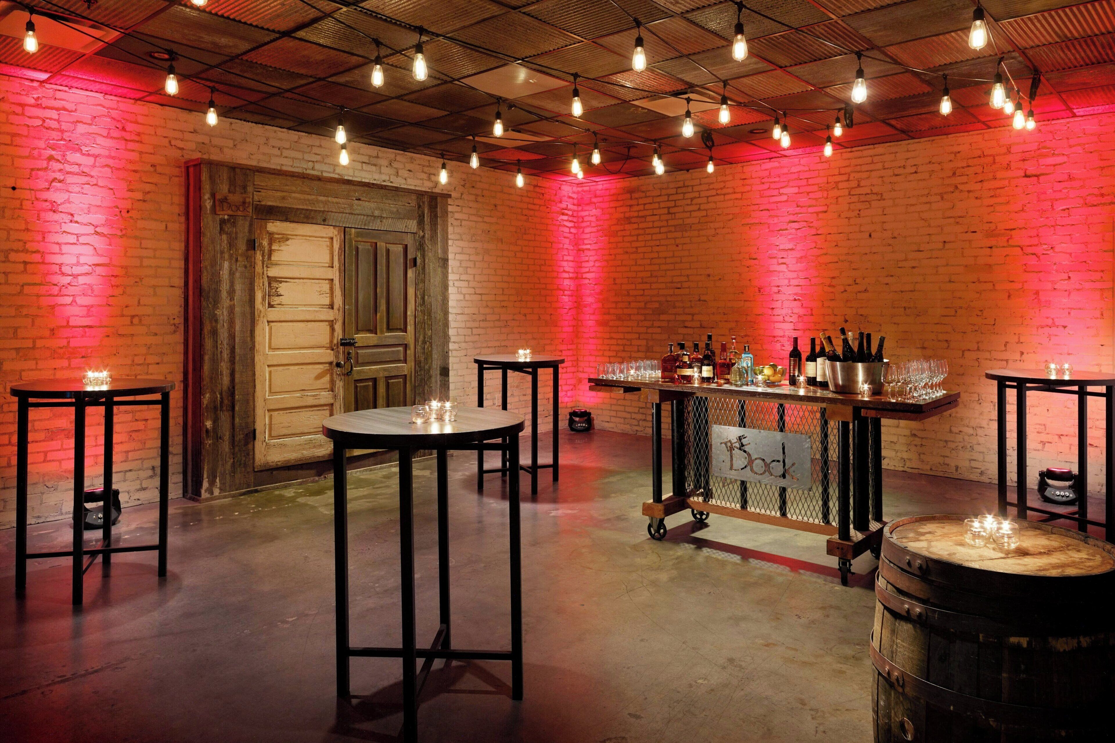 Zona de bar con mesas, taburetes y barra con botellas y vasos.