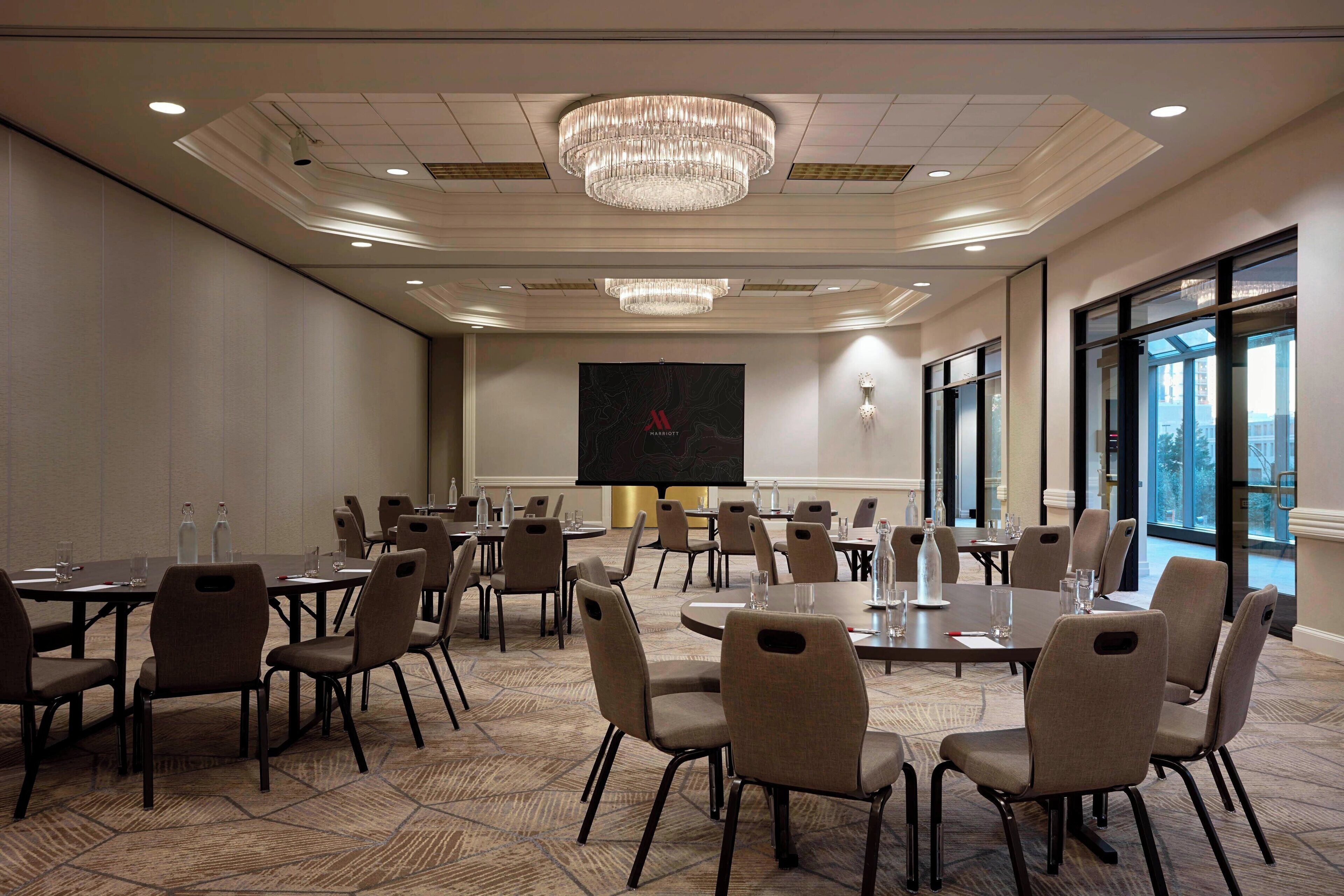 Una sala conferenze con diversi tavoli e sedie, un grande schermo e un lampadario.