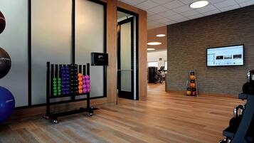 A modern gym with exercise equipment, a digital screen, and a wooden floor.