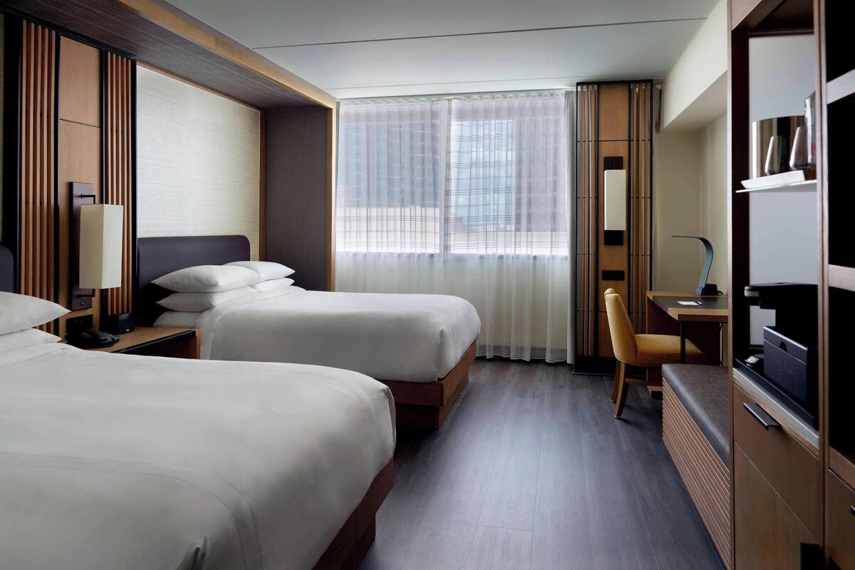 A hotel room with two beds, a desk, a chair, and a TV.