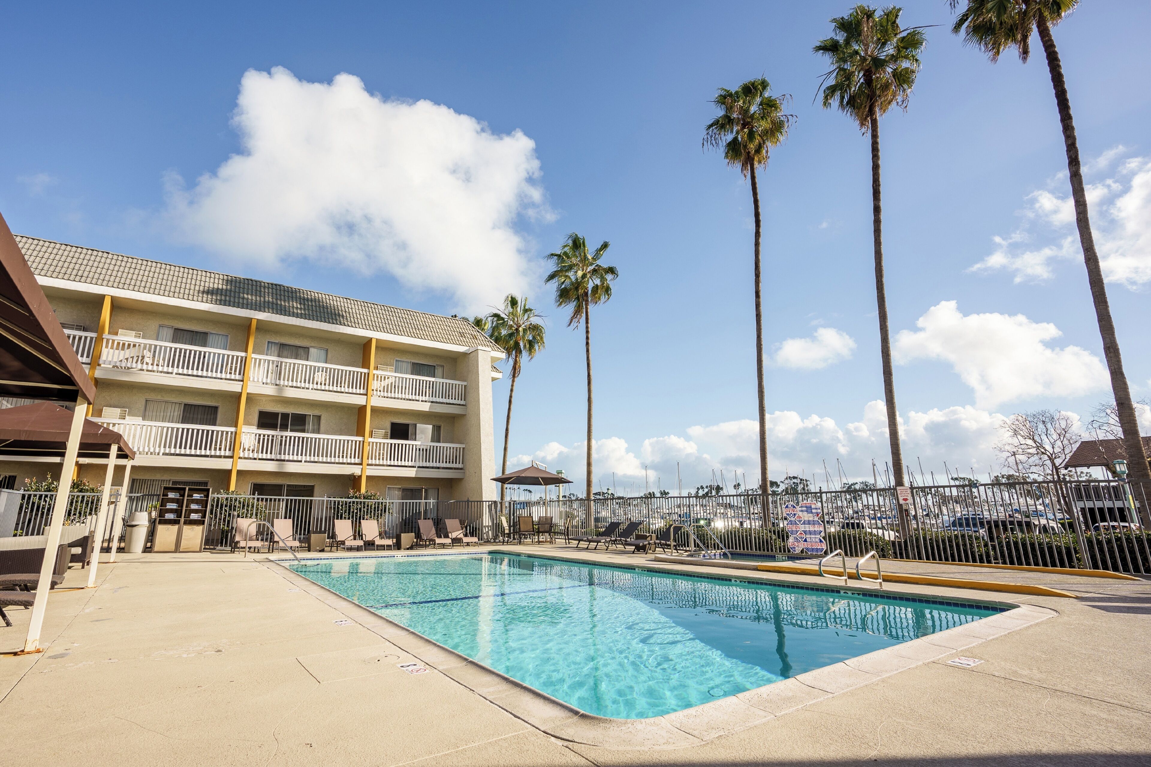 A hotel with a swimming pool, palm trees, and a fenced balcony area.