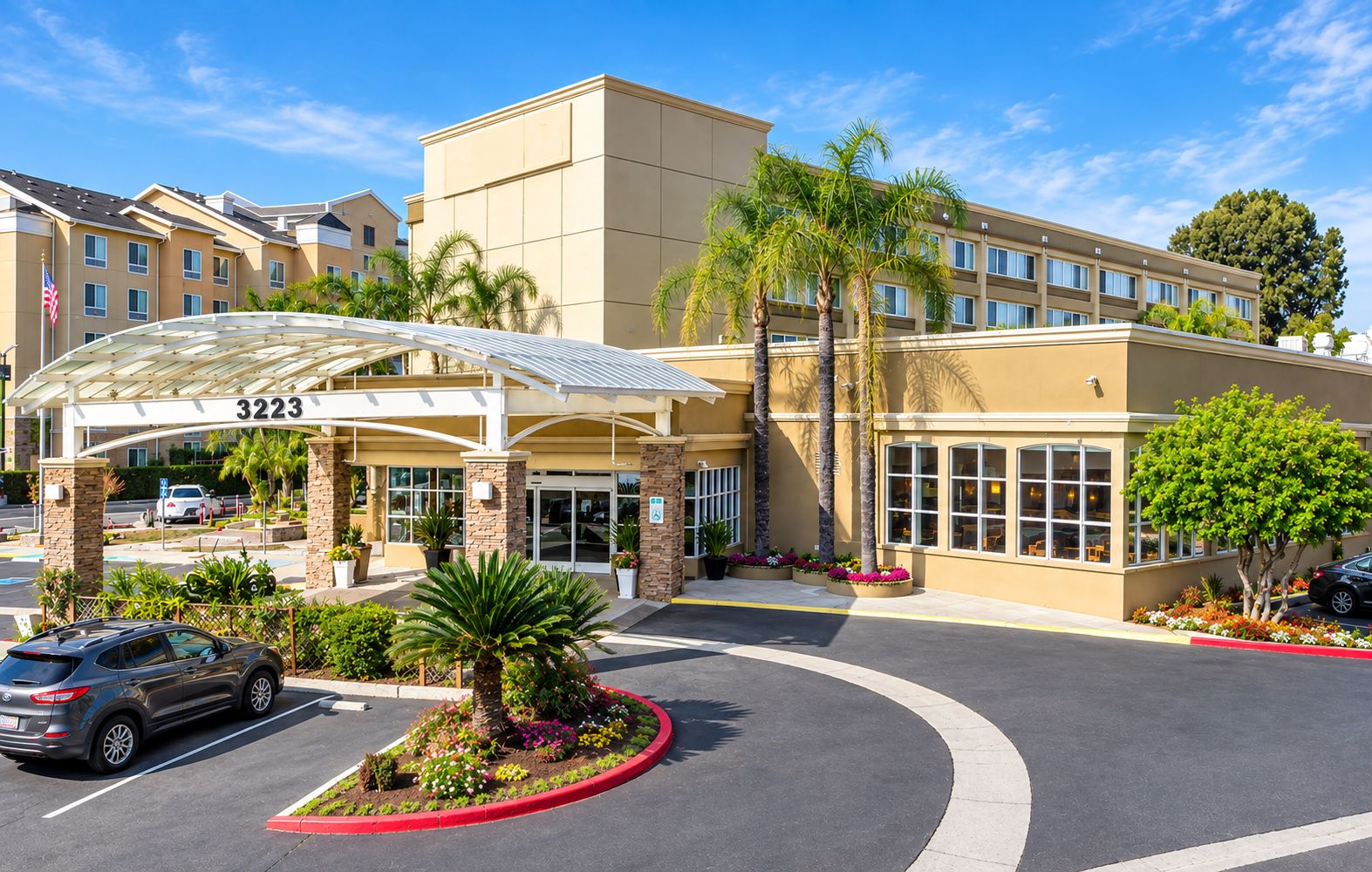 A hotel entrance with a covered walkway, palm trees, and a parking lot.