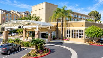 A hotel entrance with a covered walkway, palm trees, and a parking lot.
