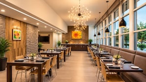 A restaurant with multiple dining tables, a central chandelier, and a view of the outdoors through large windows. - Pacific Stay Hotel (West Covina)