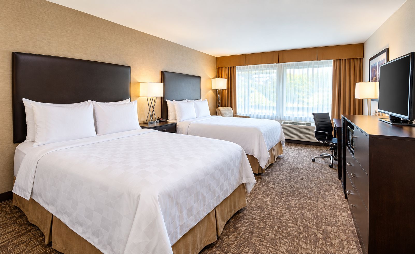 A hotel room with two beds, a desk, a television, and a window with curtains.