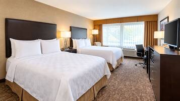 A hotel room with two beds, a desk, a television, and a window with curtains.