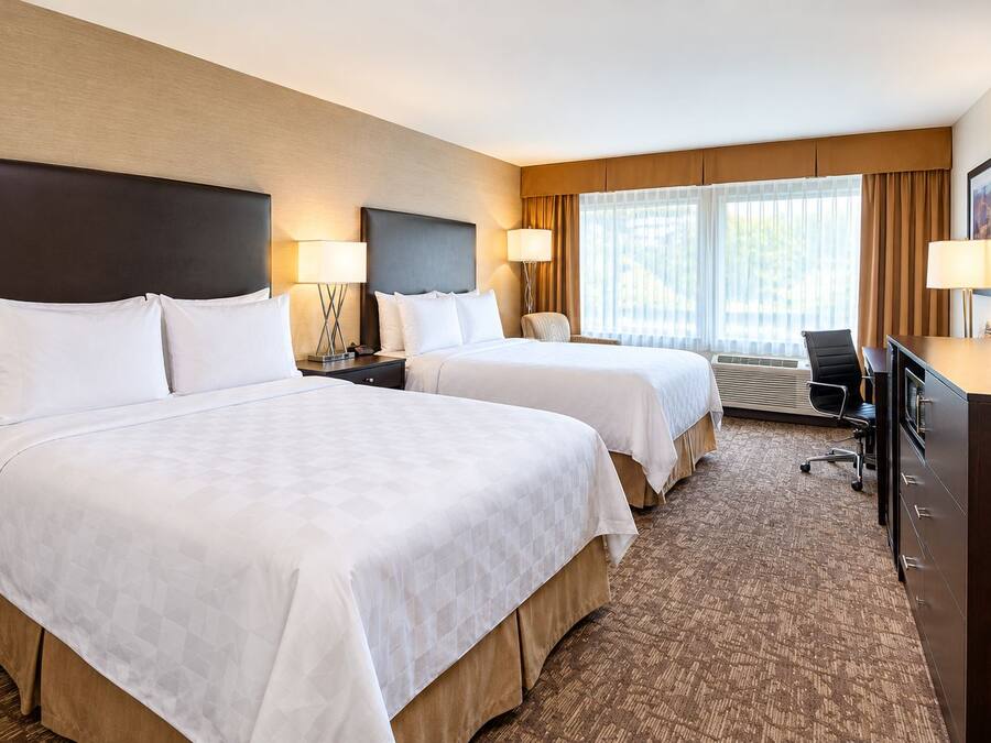 A hotel room with two beds, a desk, a television, and a window with curtains.
