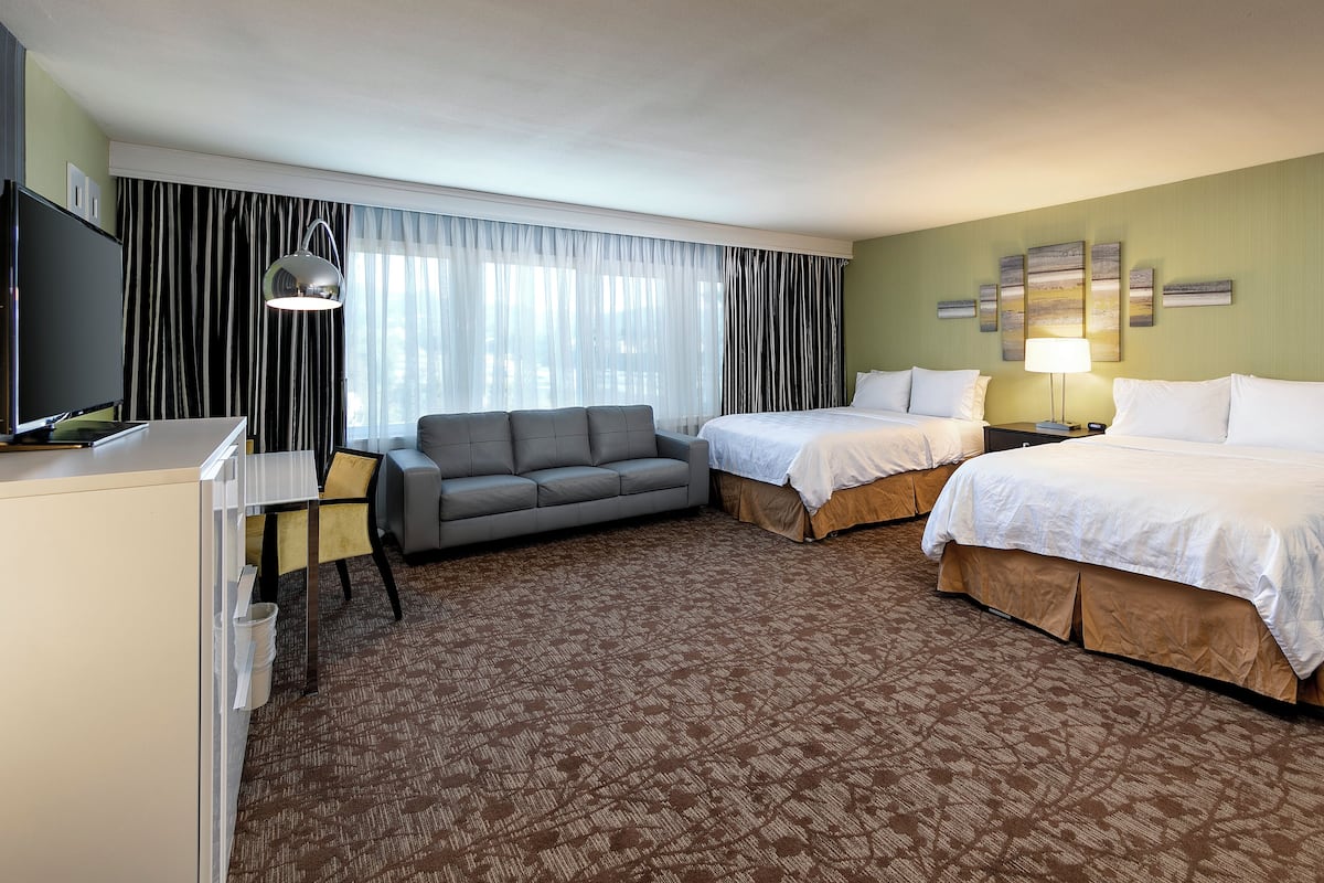 A hotel room with a sofa, two single beds, a desk with a computer, and a TV.