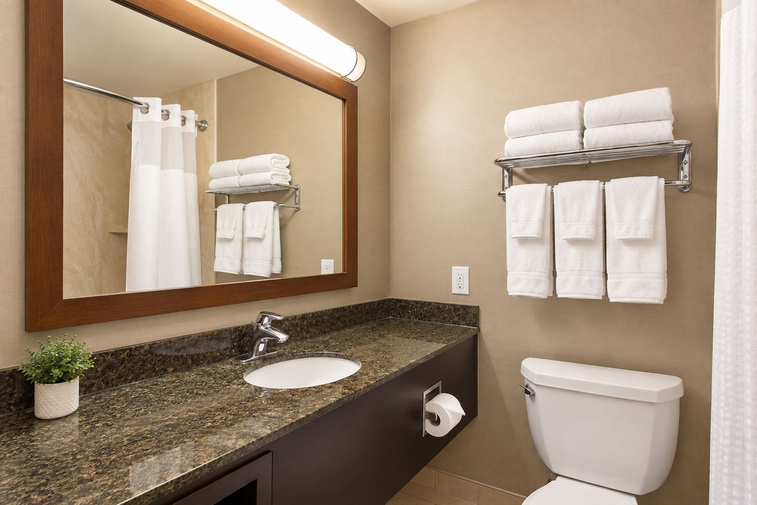 A bathroom with a granite countertop, a white sink, a mirror, a toilet, and a towel rack with folded towels.