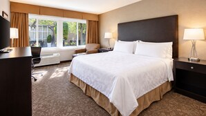 A hotel room with a large bed, a desk, a chair, a TV, and a window with curtains. - Pacific Stay Hotel (West Covina)