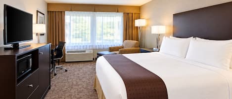 A hotel room with a large bed, a TV, a desk with a computer, and a chair.