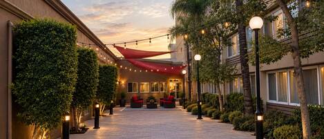 A hotel corridor with a red canopy, potted plants, and outdoor seating.