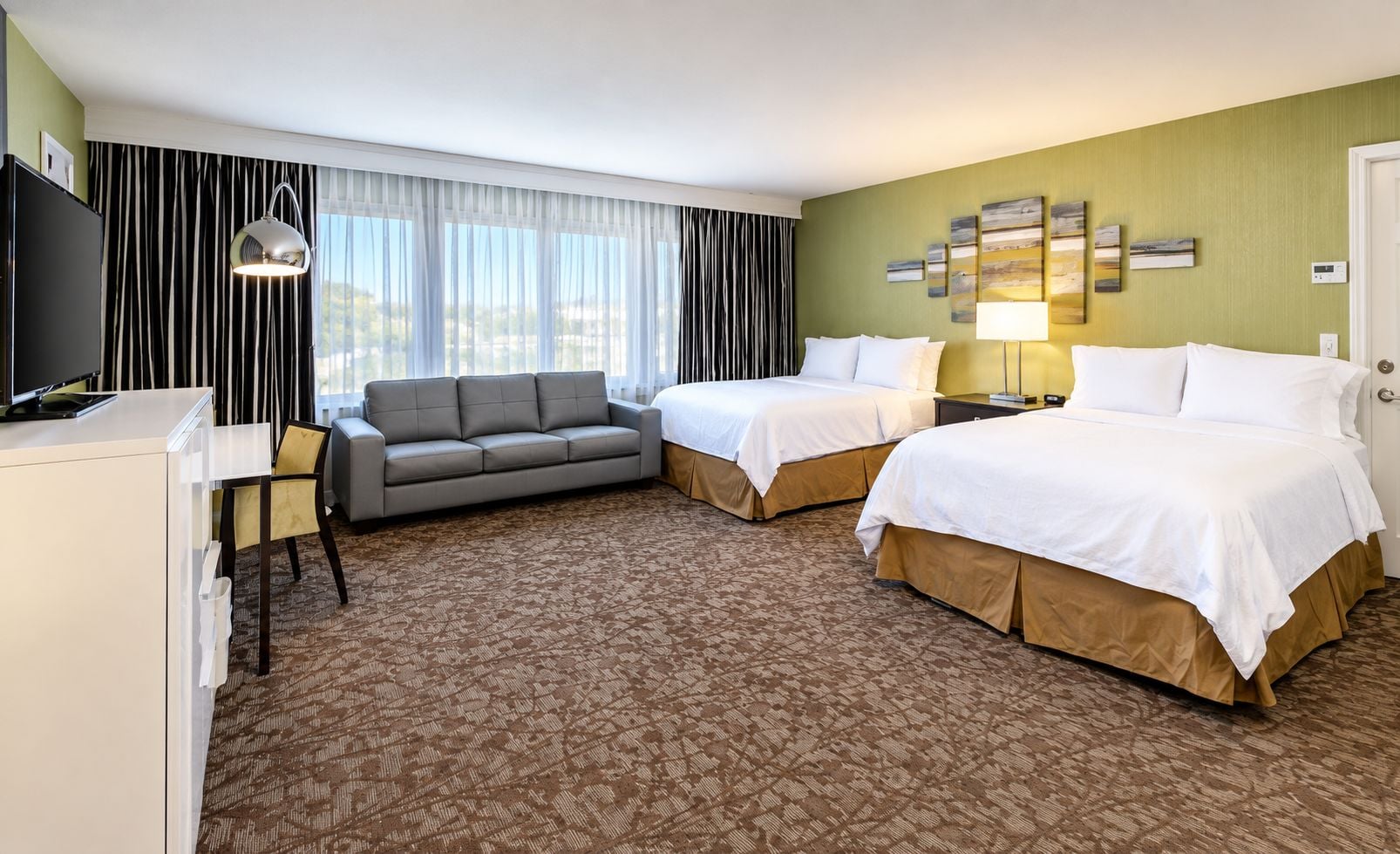 A hotel room with two beds, a sofa, a desk, and a television.