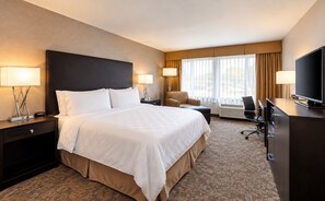 A hotel room with a large bed, two bedside tables with lamps, a desk with a chair, a television, and a window with curtains. - Pacific Stay Hotel (West Covina)
