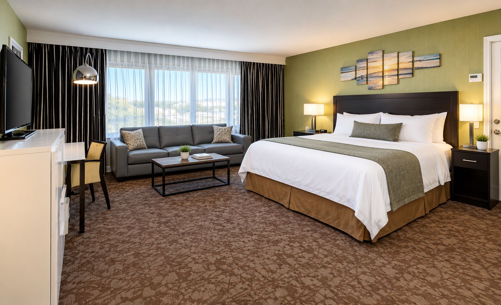 A hotel room with a bed, a sofa, a coffee table, a TV, and a desk.