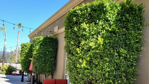 A patio area with wicker furniture and red cushions, surrounded by neatly trimmed hedges. - Pacific Stay Hotel (West Covina)
