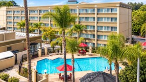 A hotel with a swimming pool, palm trees, and outdoor seating. - Pacific Stay Hotel (West Covina)