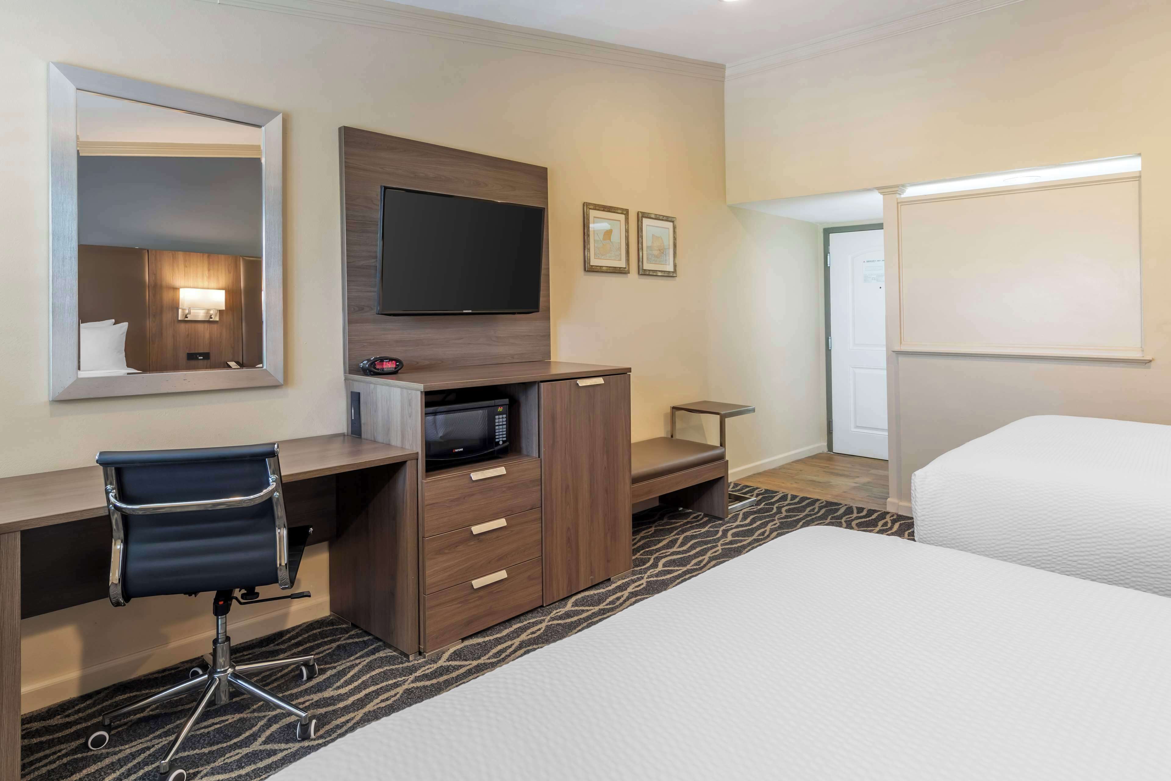 Une chambre d’hôtel comprenant un lit, un bureau avec une chaise, un téléviseur à écran plat, un four à micro-ondes et une petite table.