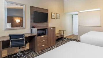 A hotel room with a bed, a desk with a chair, a flat-screen TV, a microwave, and a small table.