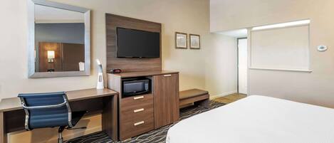 Une chambre d’hôtel comprenant un lit, un bureau avec une chaise, une télévision, un four à micro-ondes et un grand miroir.