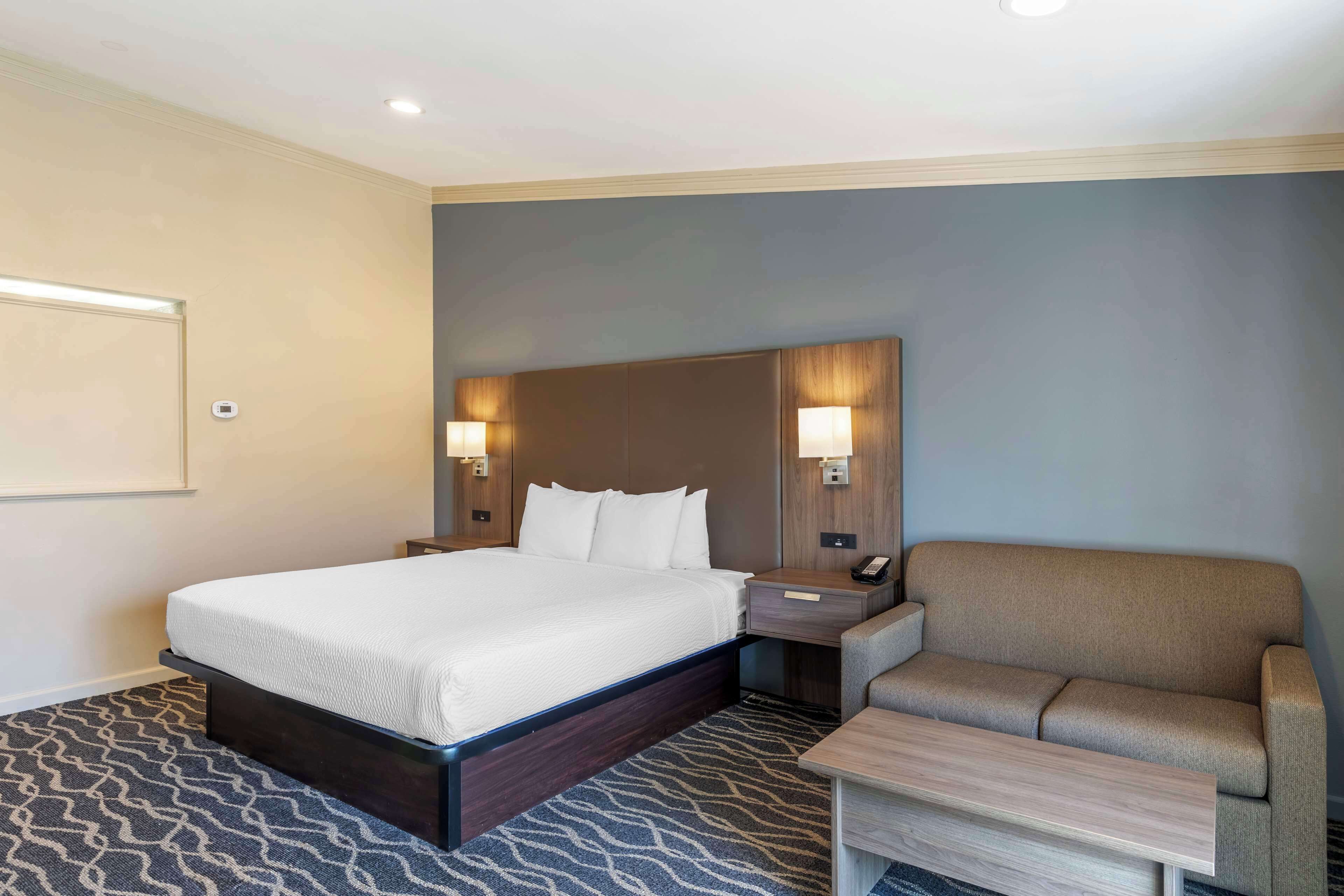 Habitación de hotel con una cama grande, un sofá, una mesita de noche con teléfono y dos lámparas de pared.