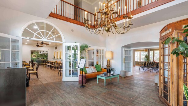 A spacious lobby with a high ceiling, wooden flooring, a chandelier, and a telephone booth. - Best Western Plus Hill House (Bakersfield)