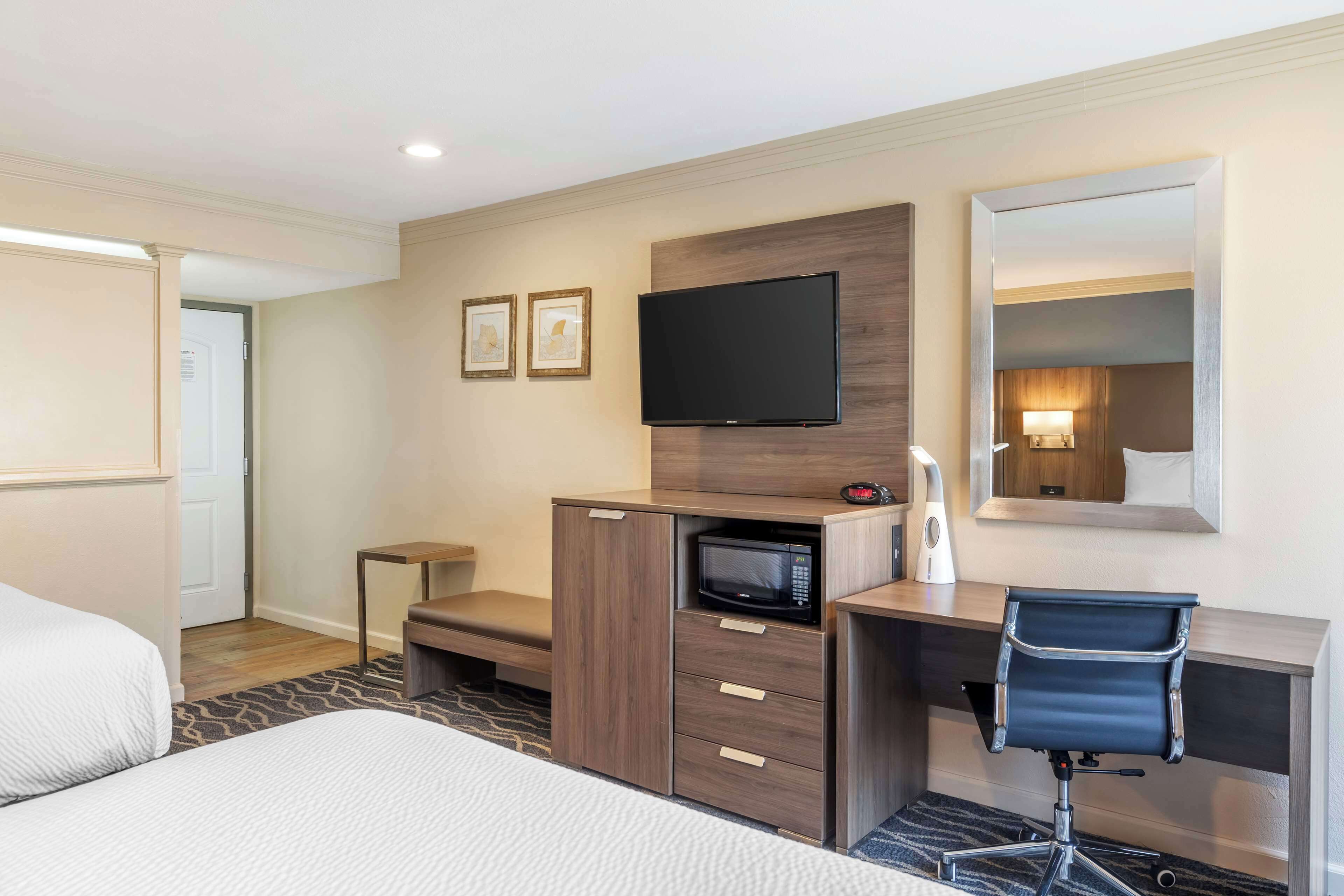 Een hotelkamer met een bed, een bureau met stoel, een magnetron, een flatscreen televisie en een spiegel.