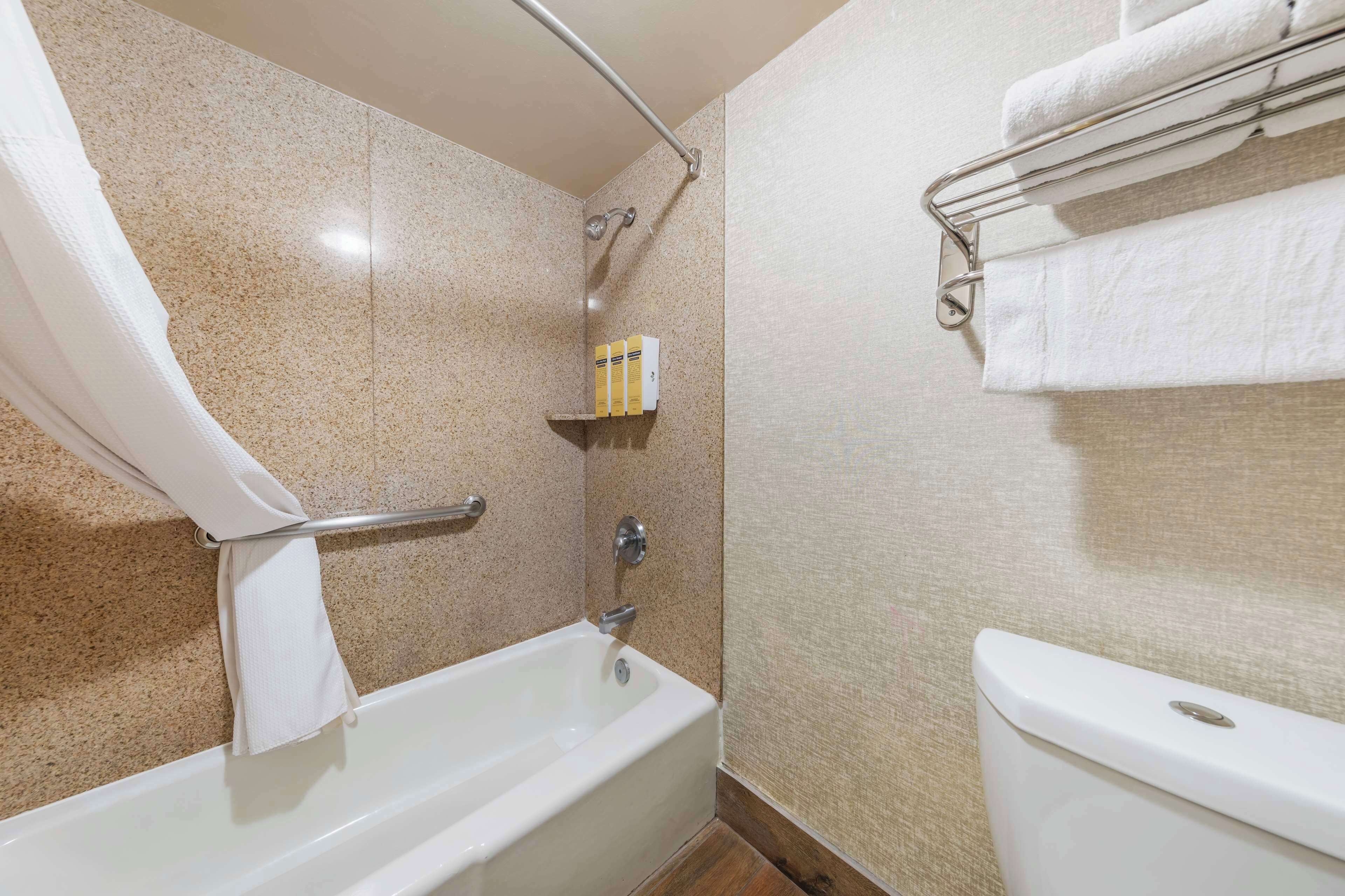 Un baño con bañera, ducha y retrete. Hay un perchero con toallas y un estante con artículos de aseo.