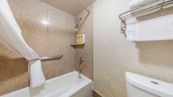 A bathroom with a bathtub, a shower, and a toilet. There is a towel rack with towels and a shelf with toiletries.