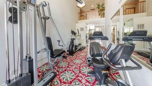 A gym with exercise equipment, a red patterned carpet, and a mirror reflecting the room. - Best Western Plus Hill House (Bakersfield)