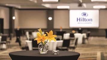 A conference room with a Hilton logo on the screen, a table with a vase of yellow flowers, and a small glass object.