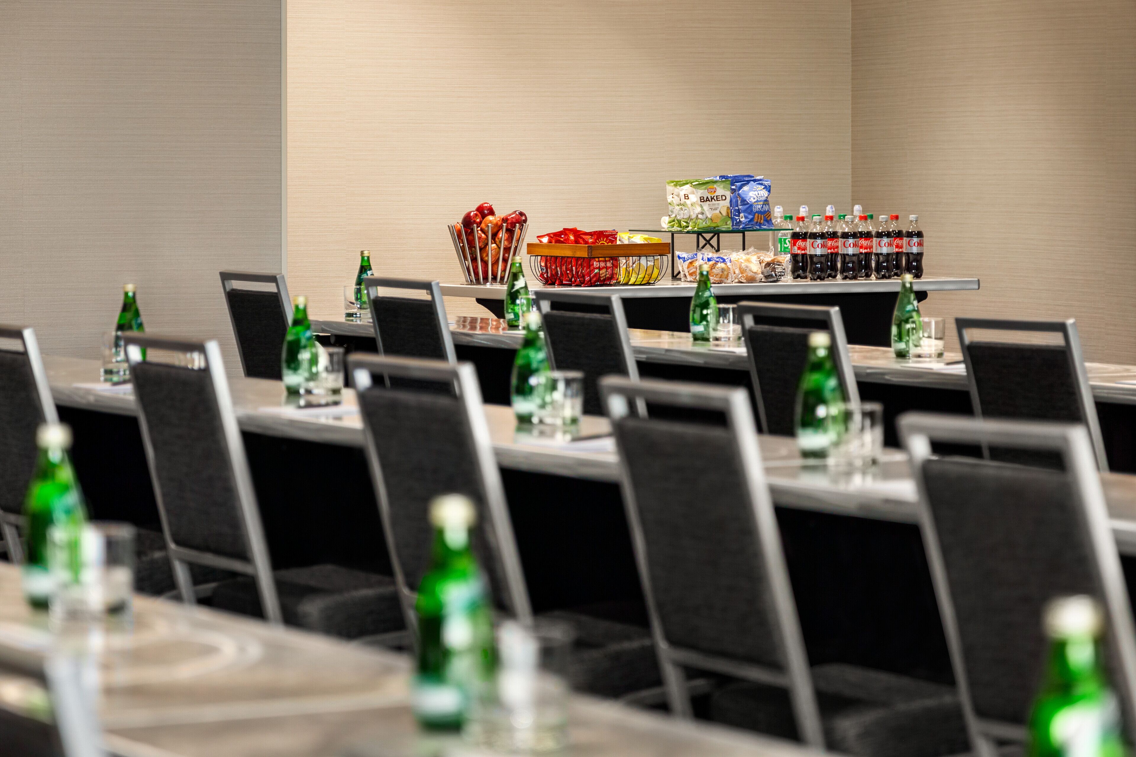 A conference room with rows of tables, each equipped with chairs, water bottles, and a snack bar with various food items and beverages.
