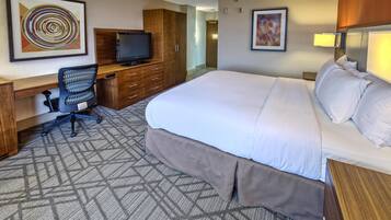 A hotel room with a large bed, a desk with a chair, a television, and artwork on the walls.