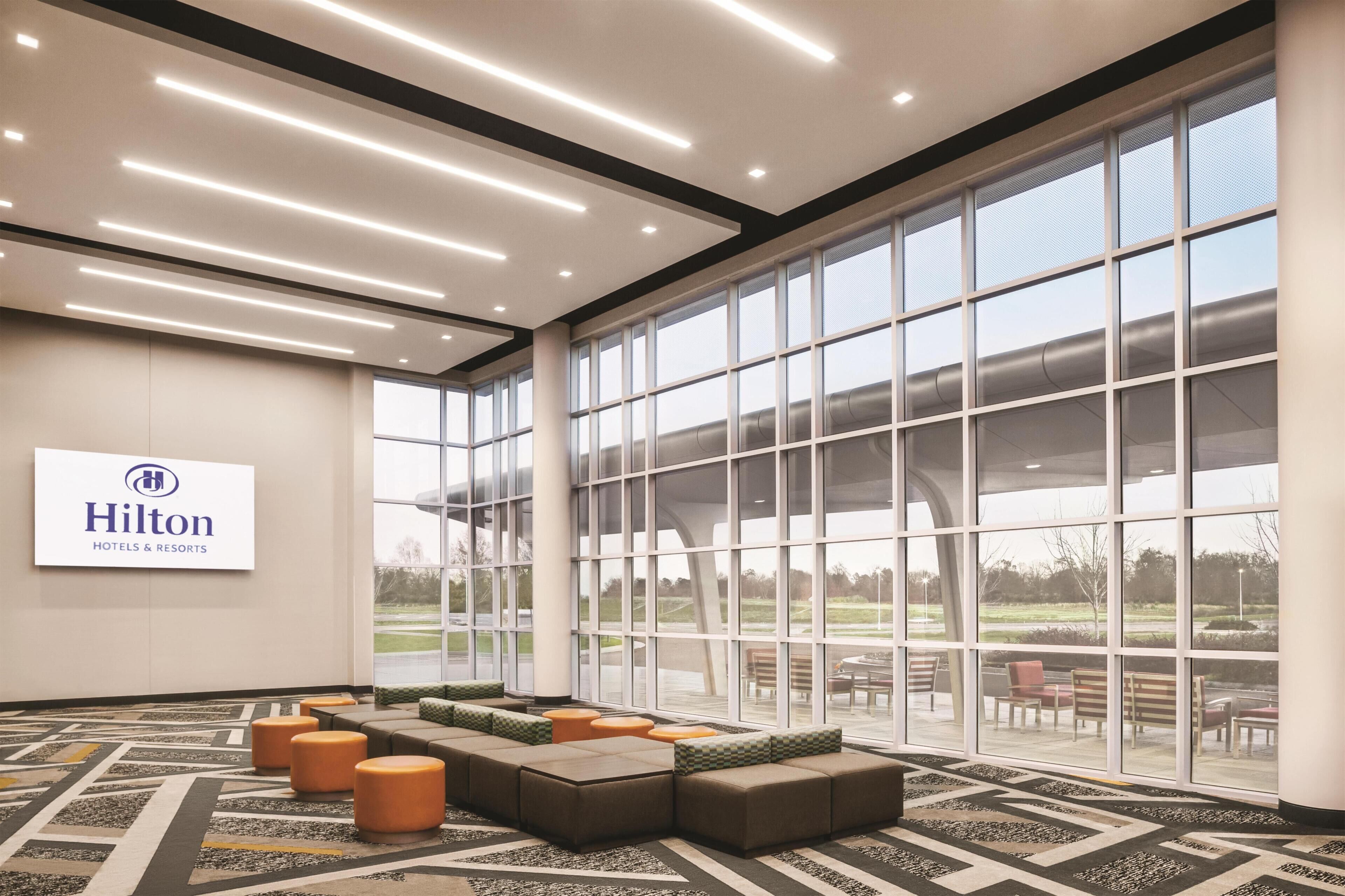 Un hall d’entrée spacieux avec un grand espace salon, une vue sur l’extérieur et un panneau indiquant les hôtels et complexes Hilton.
