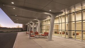 A covered outdoor seating area with chairs and tables, large windows, and a modern architectural design.