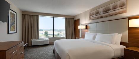 Una habitación de hotel con una cama grande, un aparador, una ventana con cortinas, un televisor montado en la pared y un cuadro.