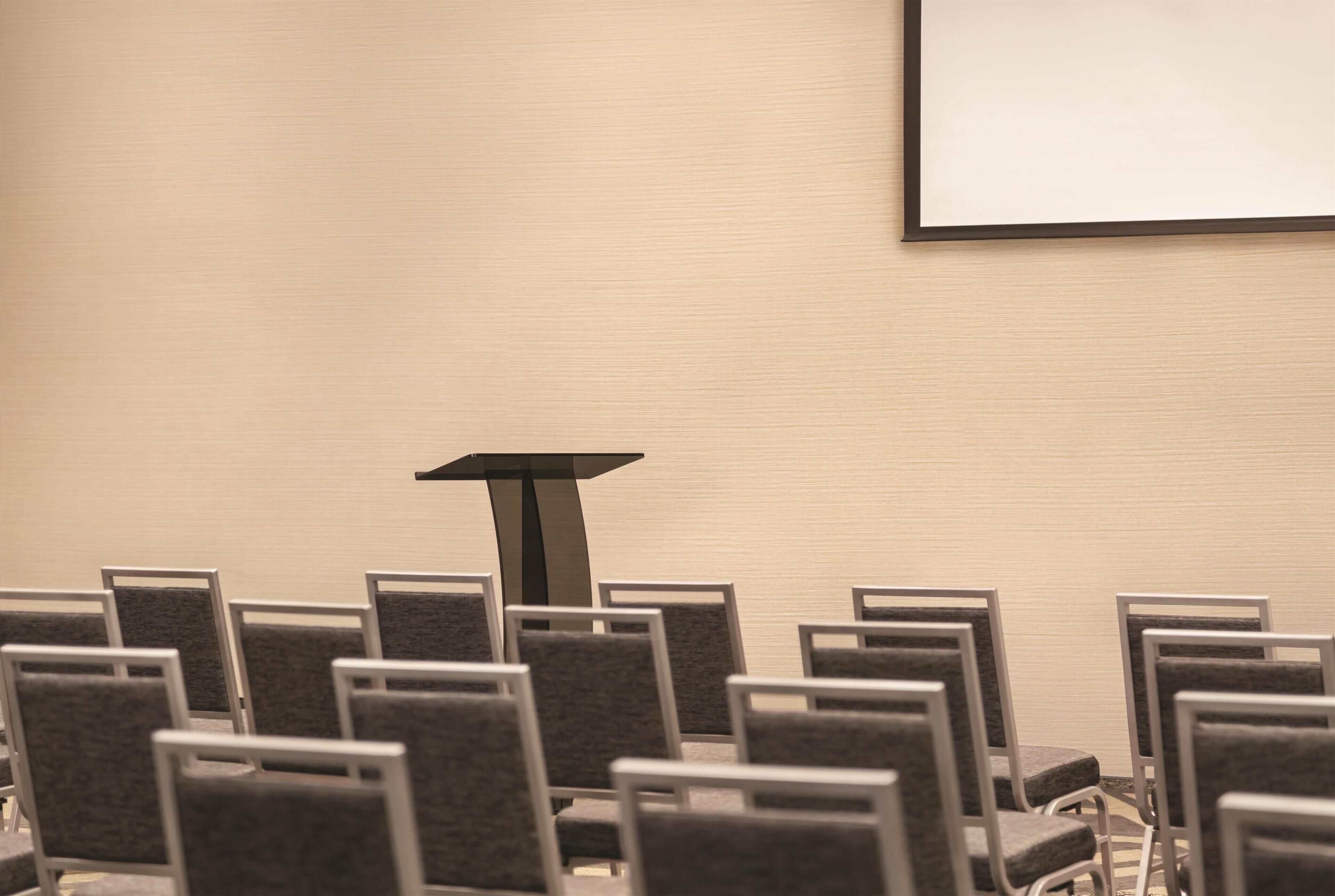 A conference room with rows of chairs, a podium, and a projection screen on the wall.