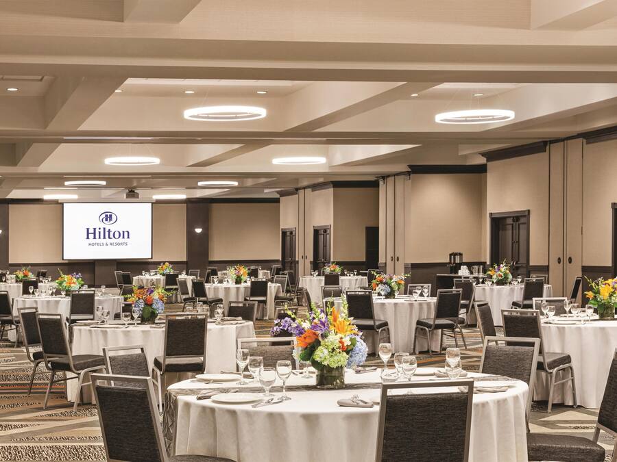 A large conference room with round tables, chairs, and floral centerpieces.