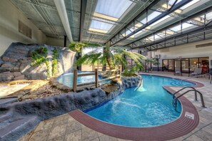 Una piscina interior con una cascada, rodeada de rocas y plantas.