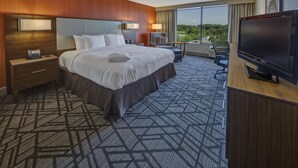 A hotel room with a large bed, a TV, a desk, and a view of the outdoors.