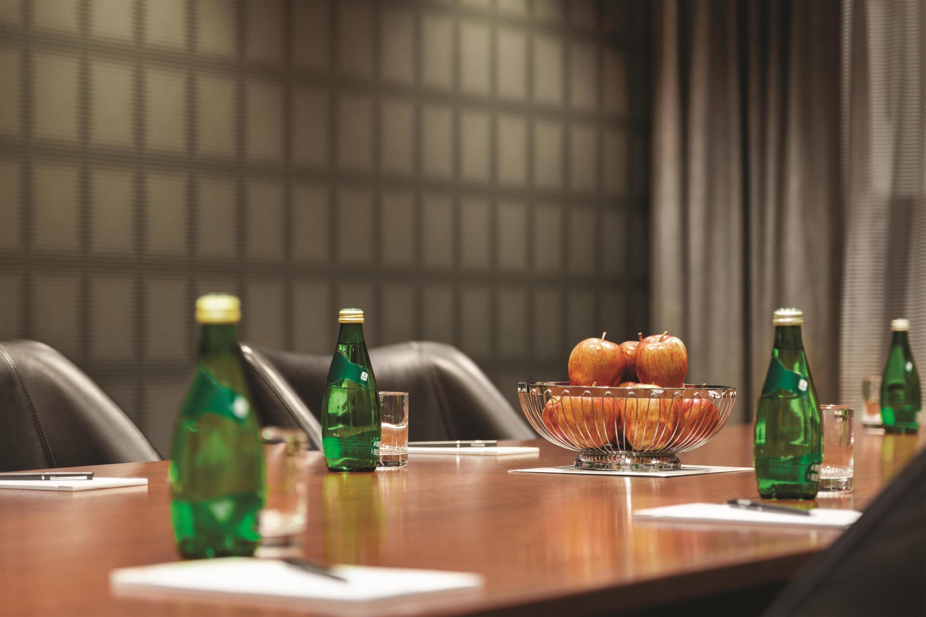 A conference table with a bowl of apples and green bottles, a notepad, and a pen.
