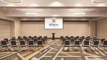 A conference room with rows of chairs, a podium, and a Hilton Hotels & Resorts logo on the wall.