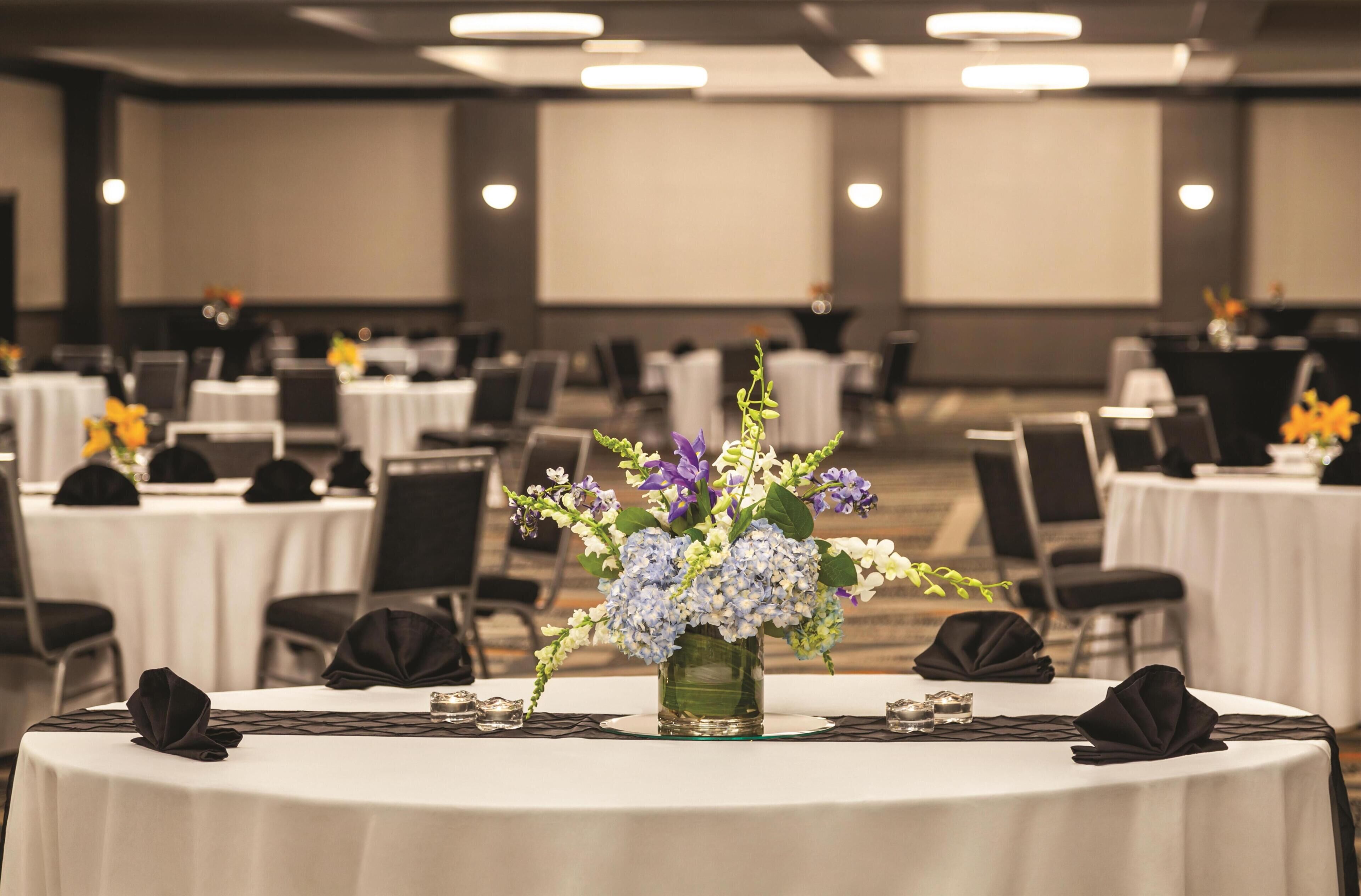 A conference room with round tables, black chairs, and a floral centerpiece.
